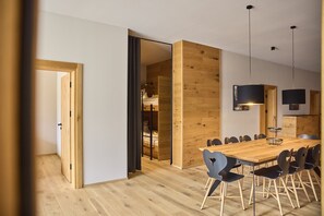 Un espace repas moderne avec une table et des chaises en bois, un luminaire suspendu noir et un mur de séparation en bois.