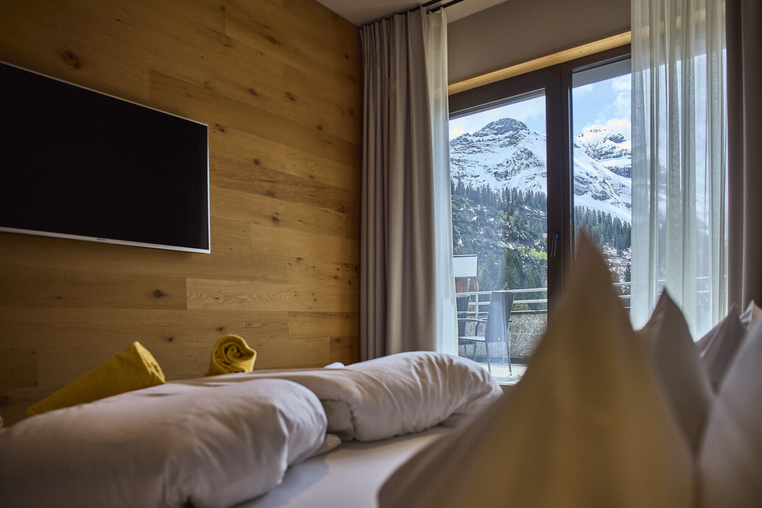 Une chambre d’hôtel avec un lit, un téléviseur fixé au mur et une fenêtre donnant sur la montagne.