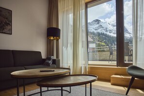 A modern hotel room with a sofa, a small table, a lamp, and a view of a snowy mountain. - 8003 Arlberg Private Retreat 3 (Schröcken)