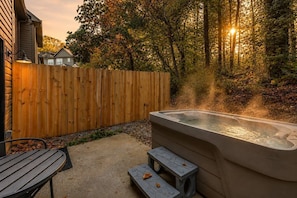 A hot tub in a backyard with a wooden fence, a bench, and a patio table. - Family-Friendly Smoky Mountain Retreat | Hot Tub (Sevierville)