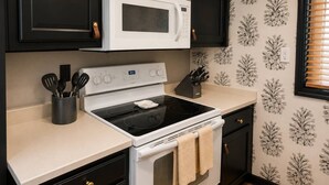 A kitchen with a white stove, black cabinets, and a microwave above it. - Family-Friendly Smoky Mountain Retreat | Hot Tub (Sevierville)