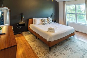 A modern bedroom with a large bed, bedside lamps, a wooden nightstand, and a view of the outdoors through a window. - Family-Friendly Smoky Mountain Retreat | Hot Tub (Sevierville)