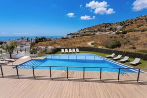 Ein Schwimmbecken mit Liegestühlen und Blick auf das Meer sowie Häuser am Hang.