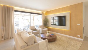 Een moderne woonkamer met een bank, fauteuils, een salontafel en een flatscreen televisie aan de muur.