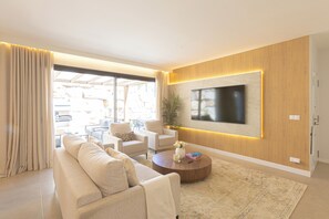Ein modernes Wohnzimmer mit einer Couch, Sesseln, einem Couchtisch und einem an der Wand befestigten Flachbildfernseher.
