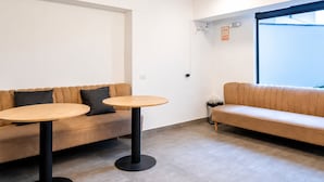Ein modernes Interieur mit einer Couch und zwei runden Tischen, einem Fenster mit Jalousien sowie einer sichtbaren Steckdose.