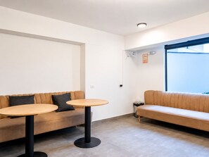 A modern interior with a sofa and two round tables, a window with blinds, and a visible electrical outlet. - Depa moderno Miraflores Gym parking 811 (Lima)