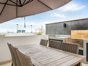 An outdoor patio with a wooden table and wicker chairs, a built-in kitchen with a sink and countertop, and a view of the city skyline. - Depa moderno Miraflores Gym parking 811 (Lima)