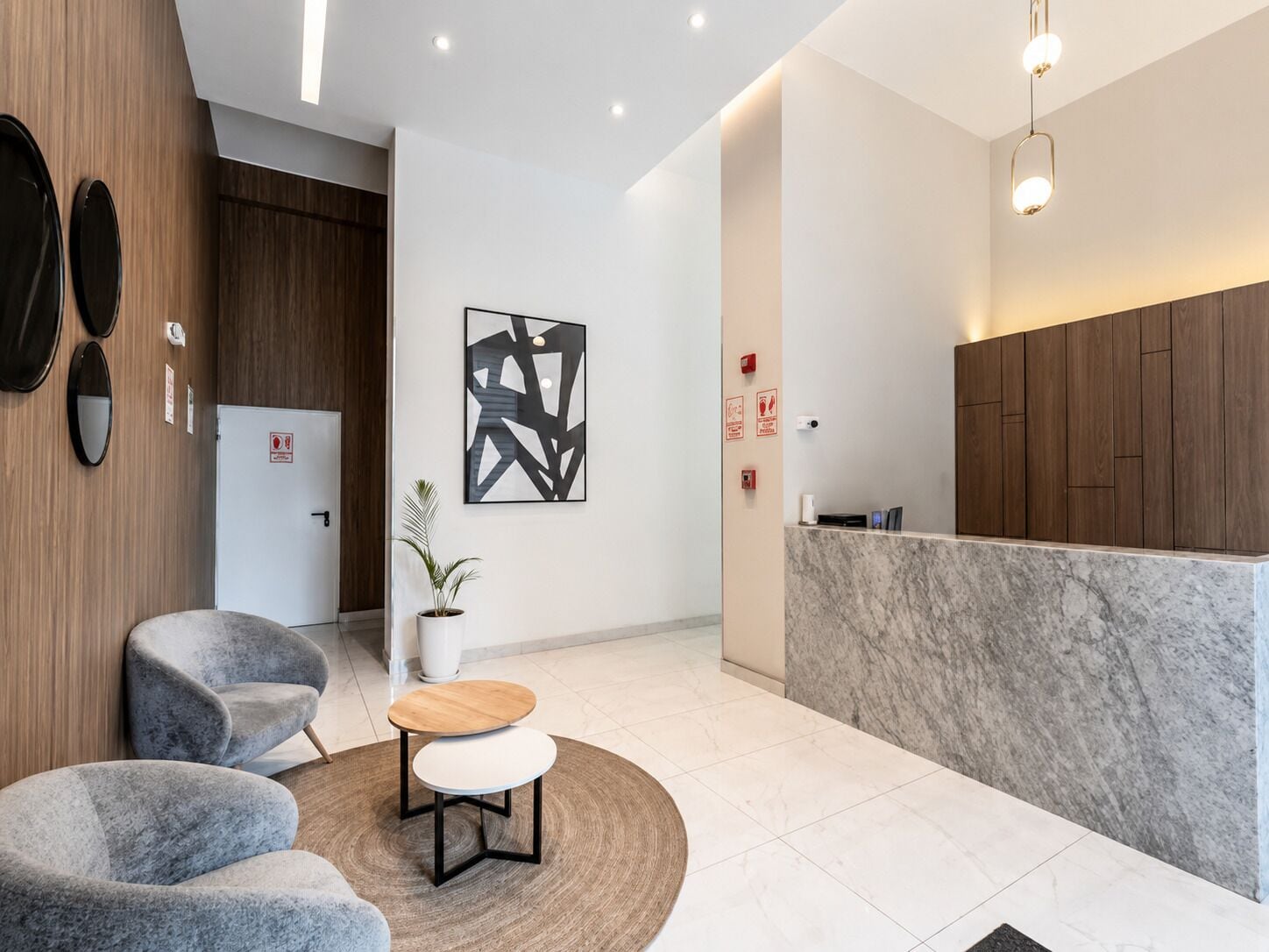 A modern reception area with a marble counter, grey upholstered chairs, a round table, and a wall-mounted abstract art piece.