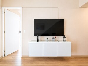 A modern living room with a flat-screen TV mounted on a white cabinet, a remote control, a small potted plant, and a candle on the cabinet. - Depa moderno Miraflores Gym parking 811 (Lima)