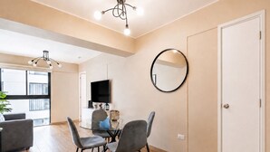 Ein modernes Wohnzimmer mit einem Glastisch, grauen Stühlen, einem Flachbildfernseher und einem runden Spiegel an der Wand.