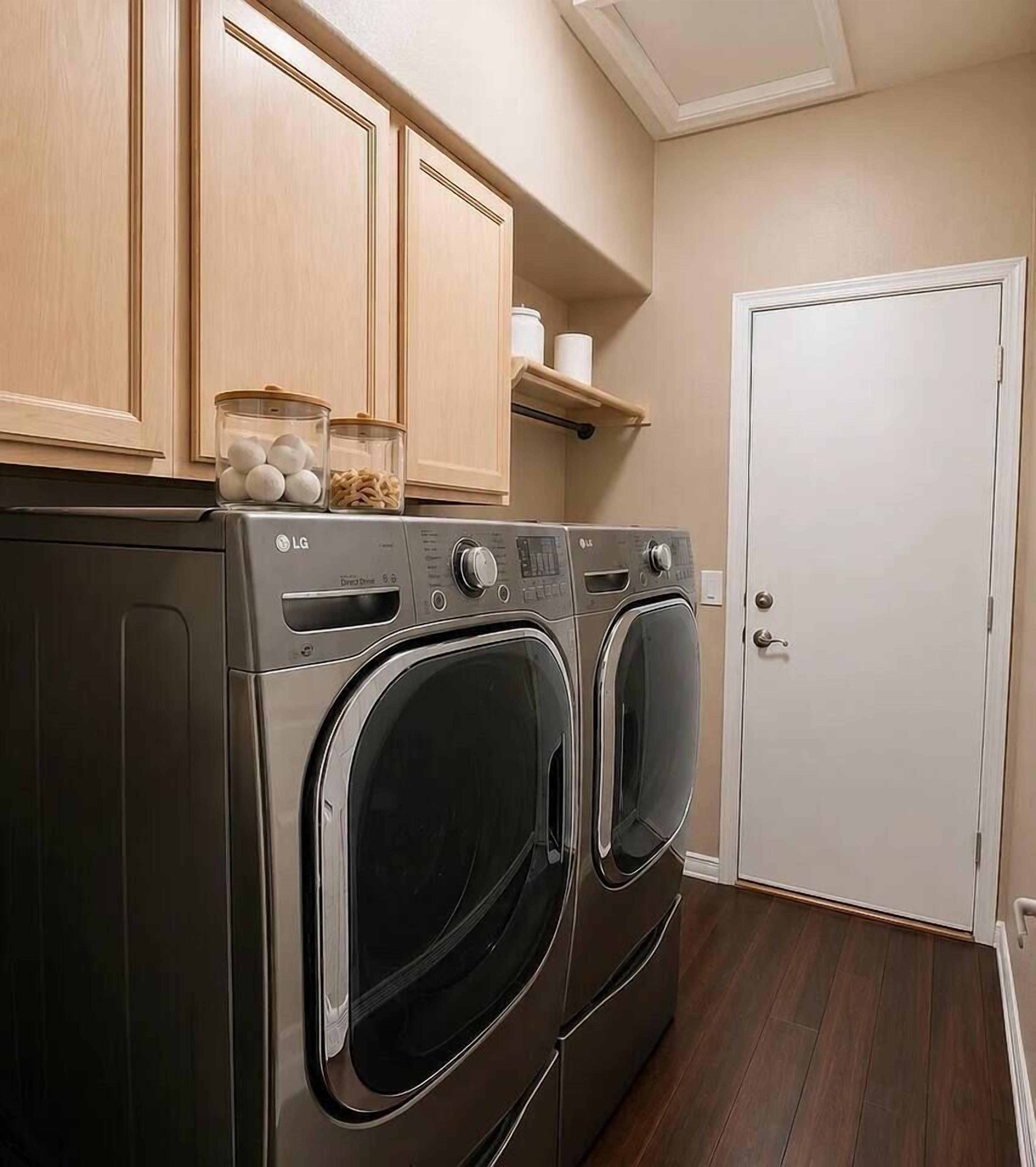 A laundry room with two front-loading LG washers, wooden cabinets, and a white door.