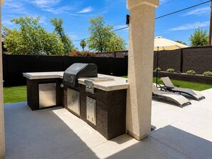 Eine Außenküche mit Grill, Spüle und Arbeitsplatte, umgeben von einer Terrasse mit Lounge-Möbeln.