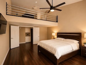 Ein Schlafzimmer mit einem großen Bett, einem Deckenventilator und Blick auf eine Küche und ein Badezimmer durch eine offene Tür.
