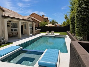 Ein rechteckiger Pool mit zwei Liegebereichen, einer mit Sonnensegel und dem anderen mit freiem Blick auf den Himmel.