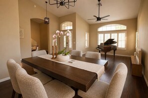Uma sala de jantar com uma mesa comprida, cadeiras, um piano e uma grande janela com persianas.