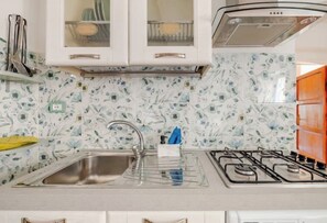 Une cuisine dotée d’un évier en acier inoxydable, d’une cuisinière à gaz et de meubles blancs avec des portes en verre.