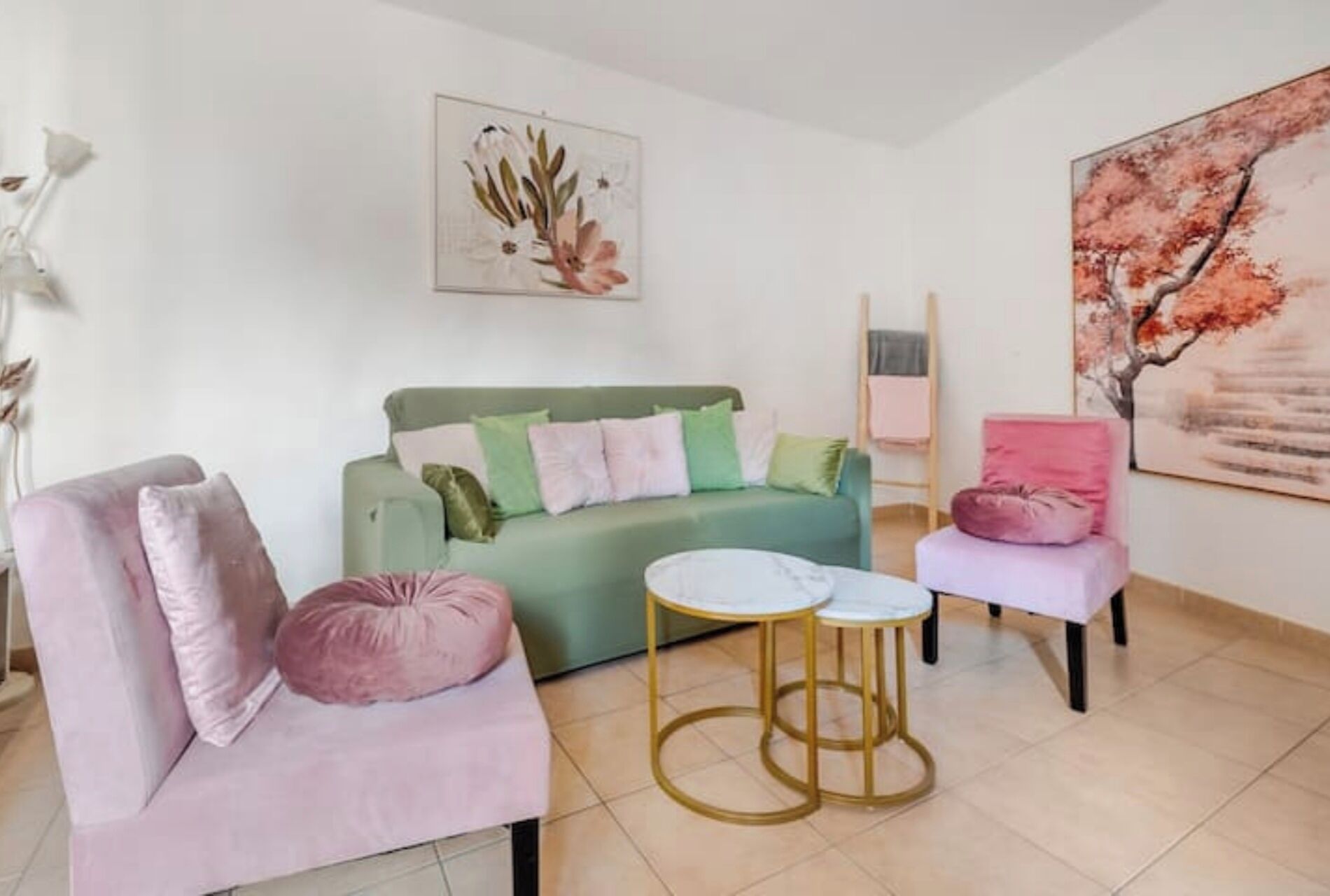 A living room with a green sofa, two pink armchairs, a small round table, and a large painting on the wall.