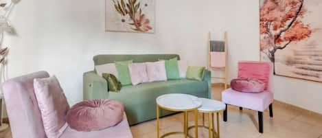 A living room with a green sofa, two pink armchairs, a small round table, and a large painting on the wall.