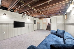 Ein Dachzimmer mit an der Wand befestigtem Fernseher, einem blauen Sofa und einer Treppe, die zu einer anderen Ebene führt.