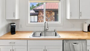 A kitchen with a stainless steel sink, white cabinets, a coffee maker, and a dishwasher. - The Copper & Pine Cottage (Anaconda)