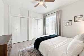 Ein Schlafzimmer mit einem Bett, einem Deckenventilator, einem Fenster mit Vorhängen und einer Kommode.