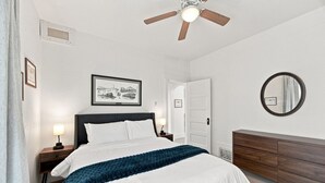 A bedroom with a bed, bedside tables, a dresser, a ceiling fan, a framed picture, and a mirror. - The Copper & Pine Cottage (Anaconda)