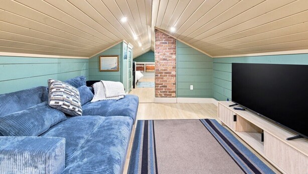 A cozy attic bedroom with a large bed, a TV, and a brick wall. - The Copper & Pine Cottage (Anaconda)