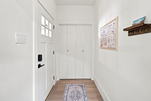 Ein Flur mit einer weißen Tür, einem an der Wand montierten Lichtschalter, einer gerahmten Karte und einem Holzregal mit Haken.