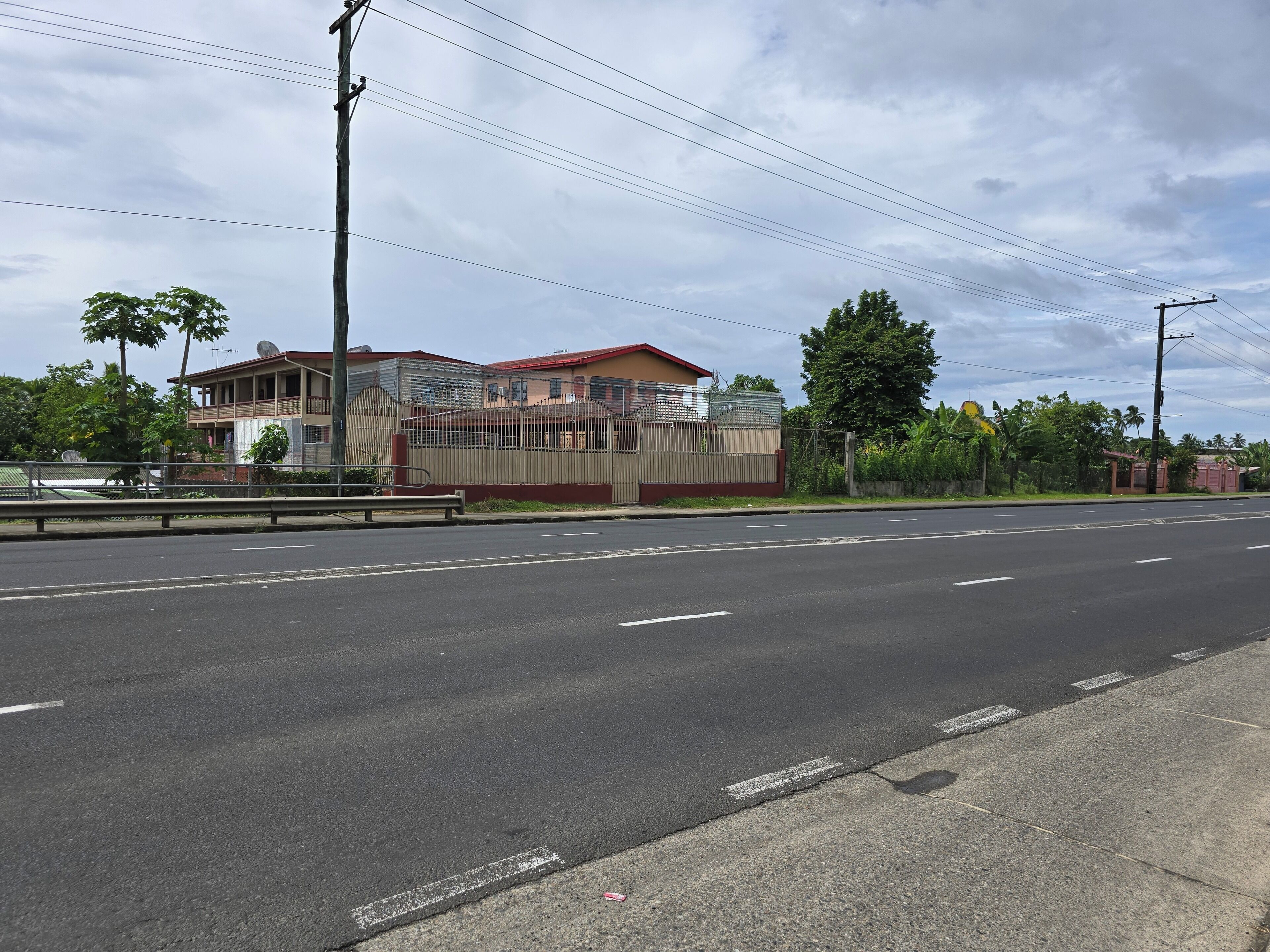 Una carretera con un edificio a la izquierda, una valla y árboles.