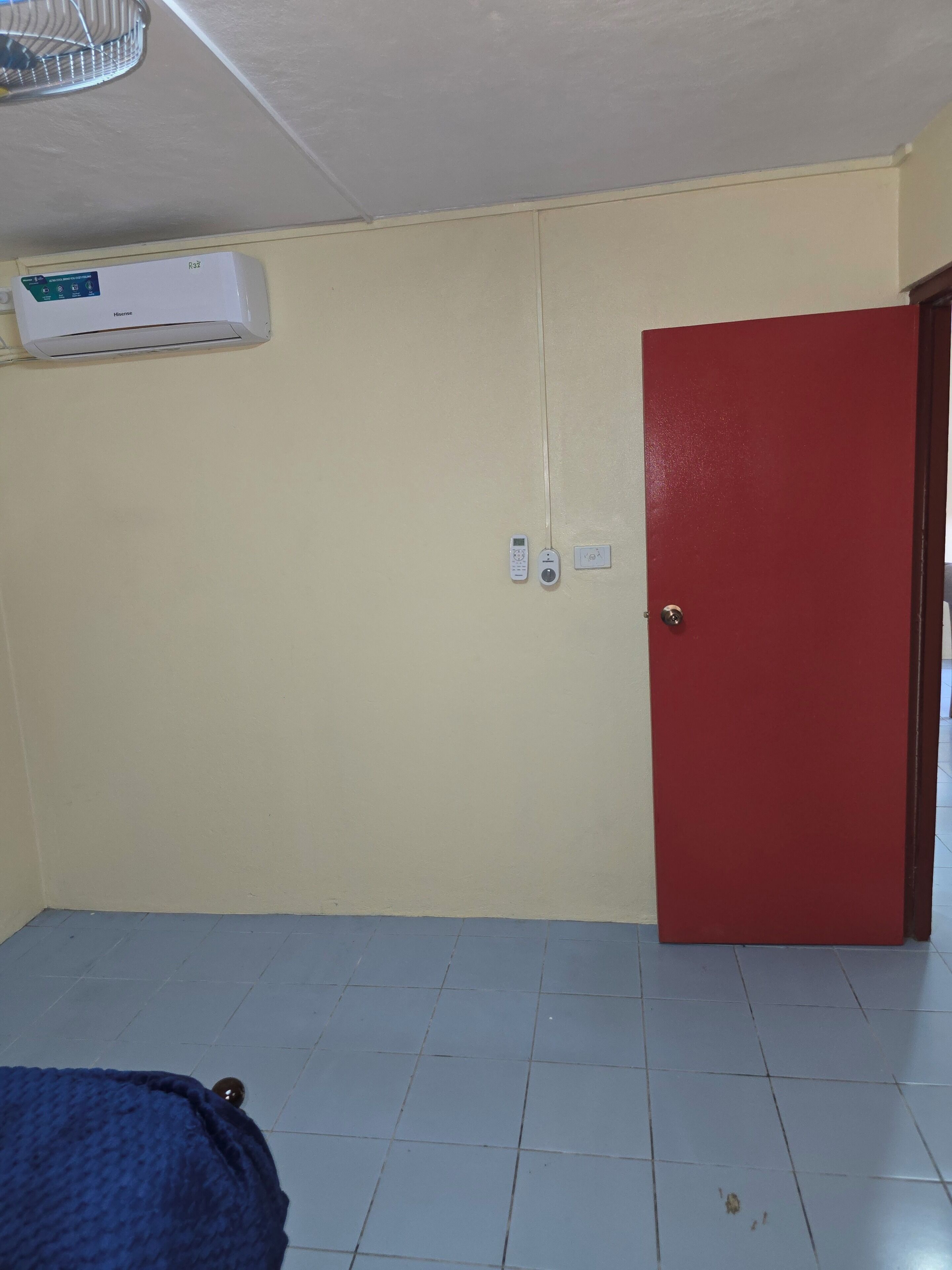 A room with a red door, an air conditioning unit on the wall, and a bed with a blue cover.