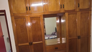 Un dormitorio con un armario de madera grande, una cama con manta azul y un ventilador de techo.
