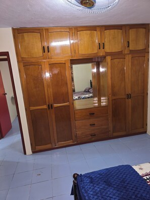 A bedroom with a large wooden wardrobe, a bed with a blue blanket, and a ceiling fan.