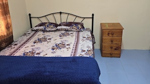 A bed with a floral bedspread, a blue blanket, and a wooden nightstand with drawers.
