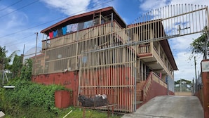 Un edificio de varios pisos con una entrada protegida por una reja, una escalera y un balcón con ropa tendida.