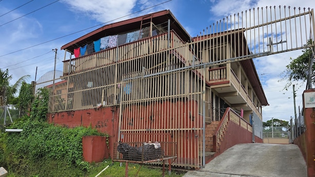 A multi-story building with a gated entrance, a staircase, and a balcony with clothes hanging.
