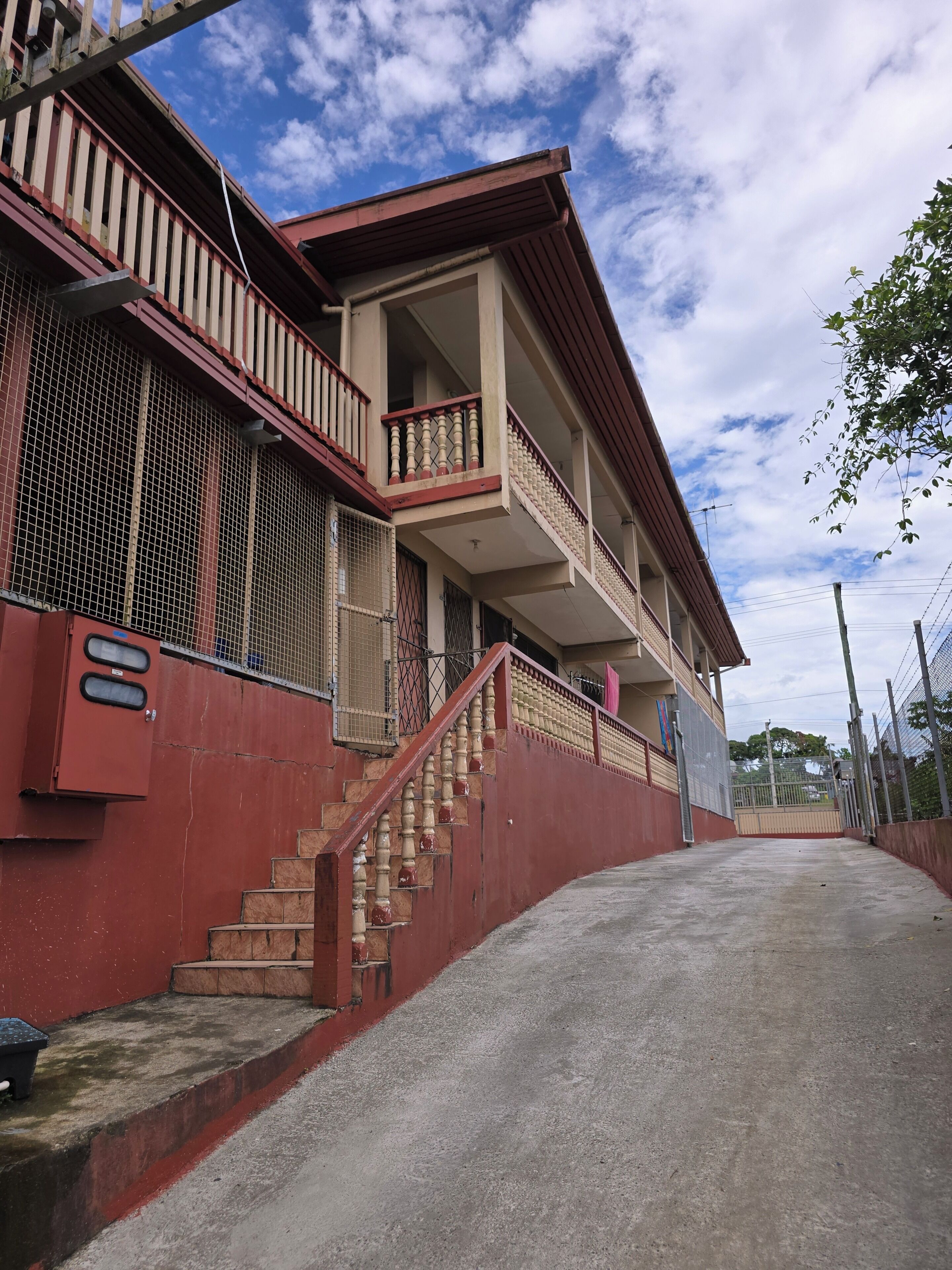 Um edifício de vários andares com fachada vermelha, uma escadaria que leva ao andar superior e uma entrada gradeada.