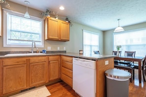A kitchen with wooden cabinets, a dishwasher, and a dining area with a table and chairs. - First Street Fanatics (Bloomington)