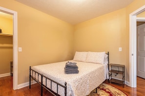 A bedroom with a bed, a nightstand, and a door. - First Street Fanatics (Bloomington)