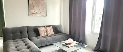 A modern living room with a grey sectional sofa, a glass coffee table, and a wall-mounted air conditioner.