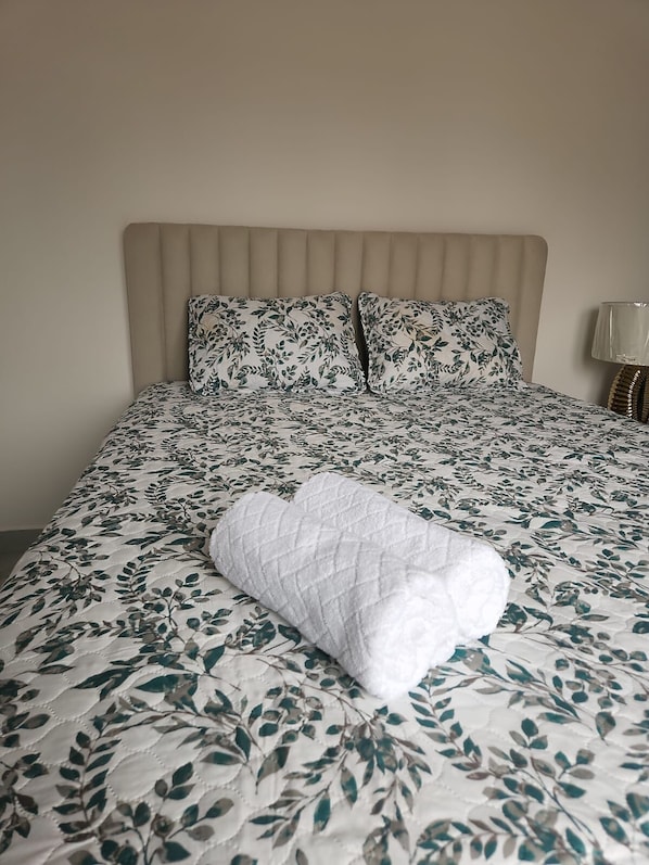 A bed with a floral bedspread and two pillows, a bedside lamp, and a folded white blanket.