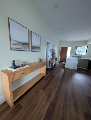 Ein modernes Interieur mit einem Holzkonsolentisch, zwei abstrakten Gemälden und einem Flur, der in einen Küchenbereich führt.