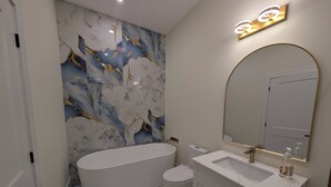 Ein modernes Badezimmer mit einer freistehenden Badewanne, einem Waschtisch mit Spiegel und einer Wand mit Marmoroptik.