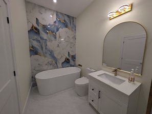 Ein modernes Badezimmer mit einer freistehenden Badewanne, einem Waschtisch mit Spiegel und einer Wand mit Marmoroptik.