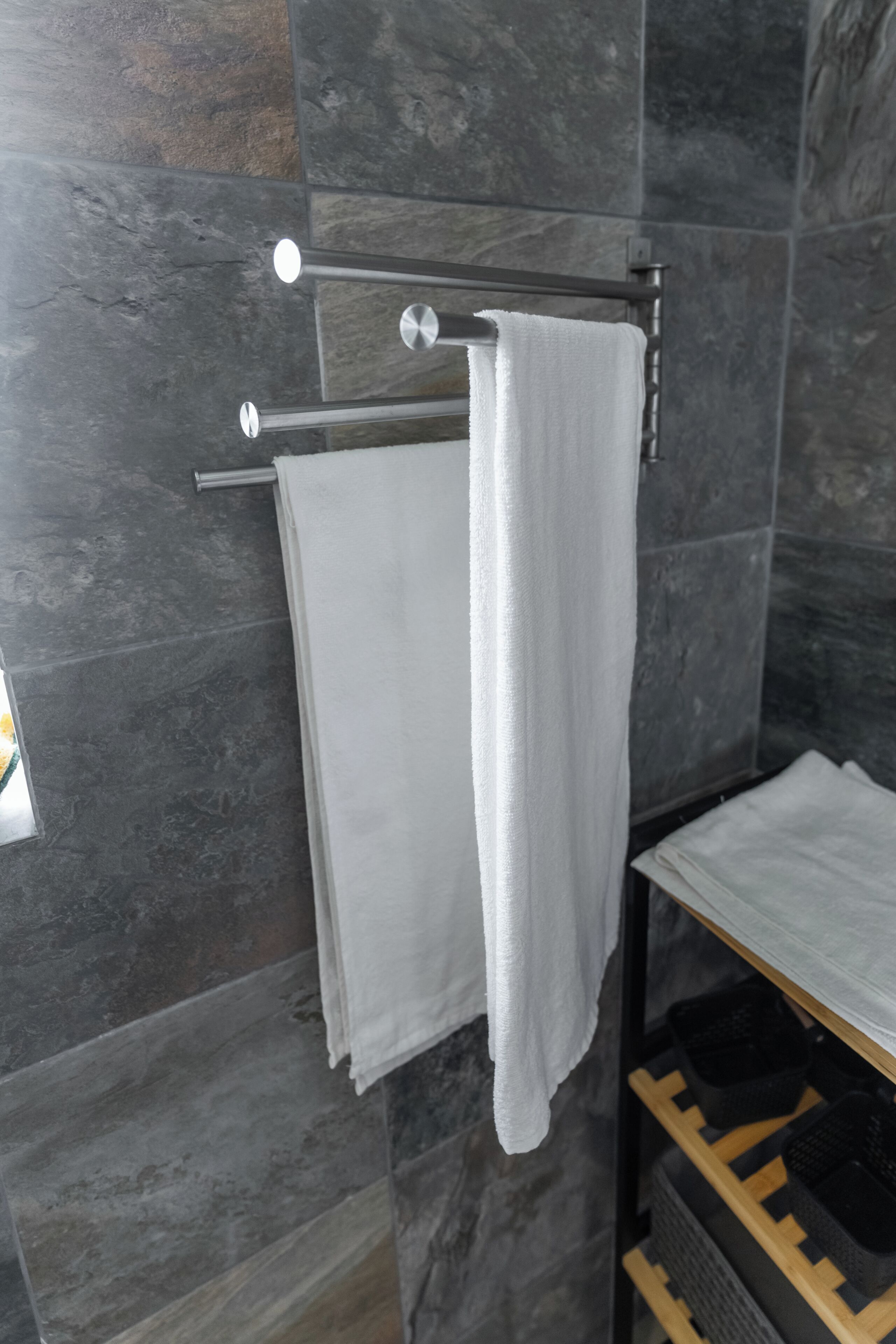 Une salle de bain avec un porte-serviettes sur lequel sont posées deux serviettes blanches, un miroir et une étagère sur laquelle se trouve un objet noir.