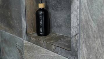 A black bottle with a pump dispenser labeled 'GEL DOUCHE' in a recessed stone wall alcove.