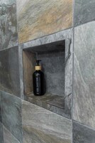 Uma garrafa preta com dosador de bomba rotulada como 'GEL DOUCHE' em um nicho de parede de pedra.