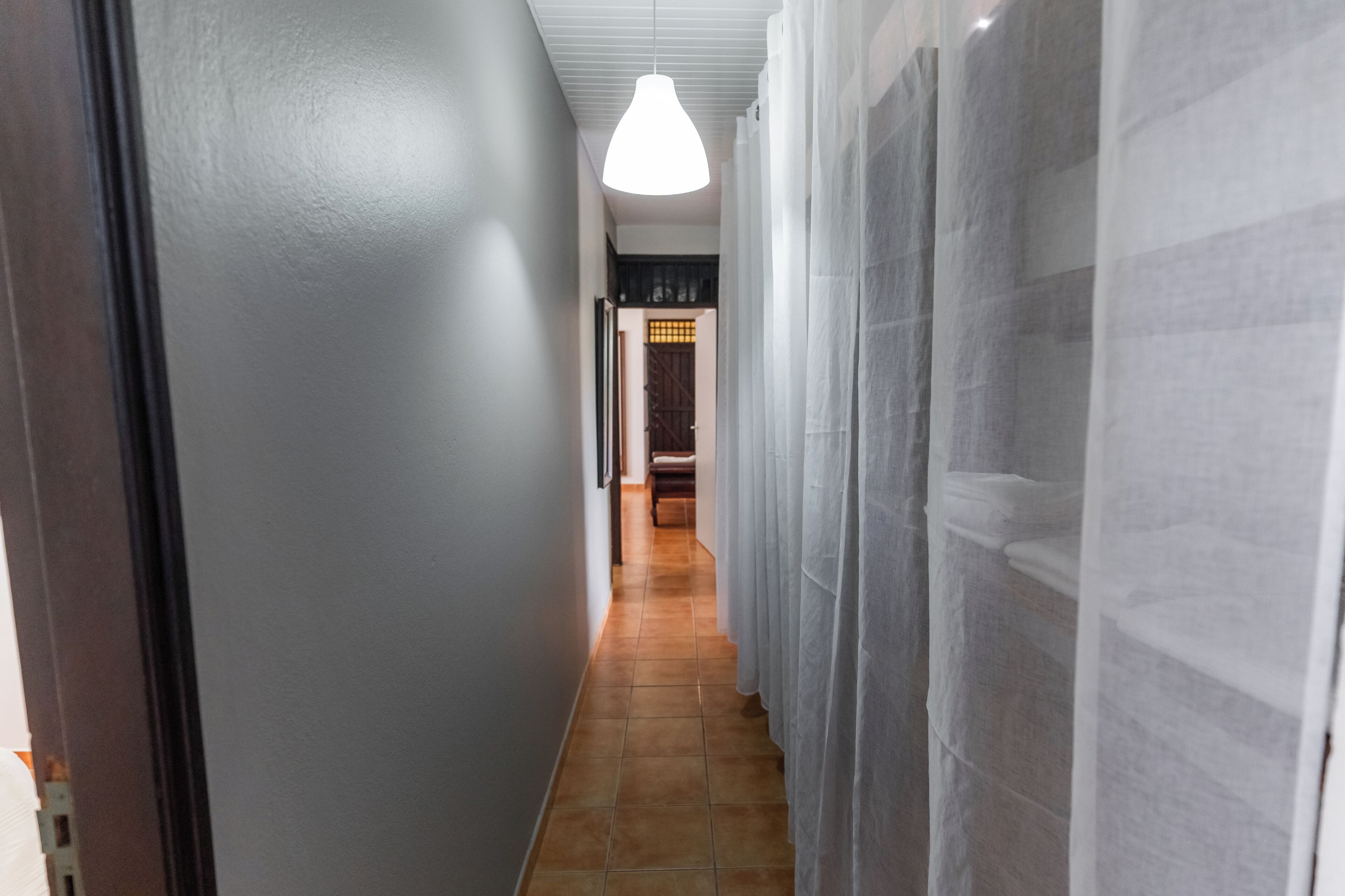 A hallway with a tiled floor, a hanging light fixture, and a door at the end.