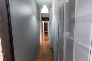 A hallway with a tiled floor, a hanging light fixture, and a door at the end.