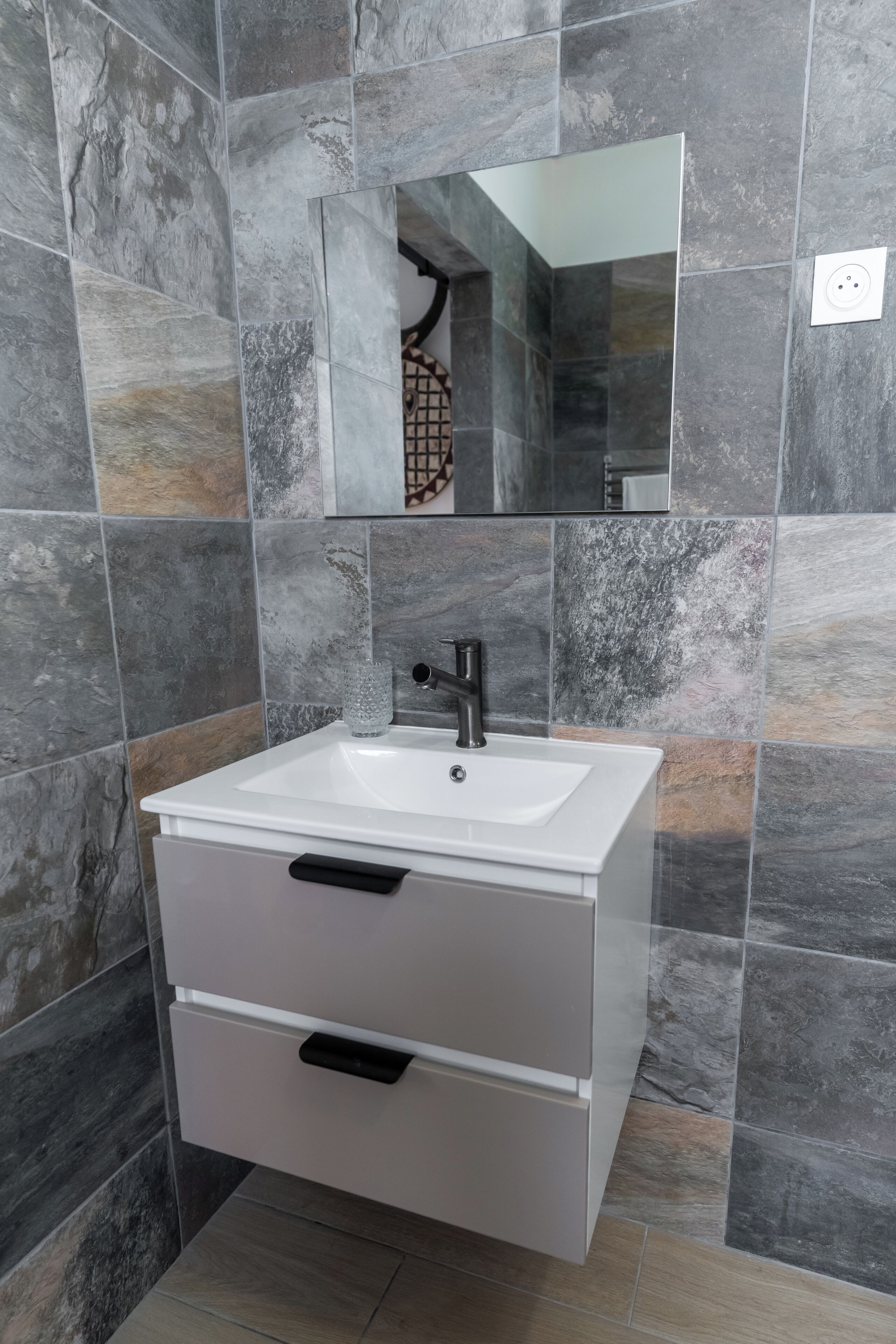 A bathroom with a white sink, a mirror, and a tiled wall.